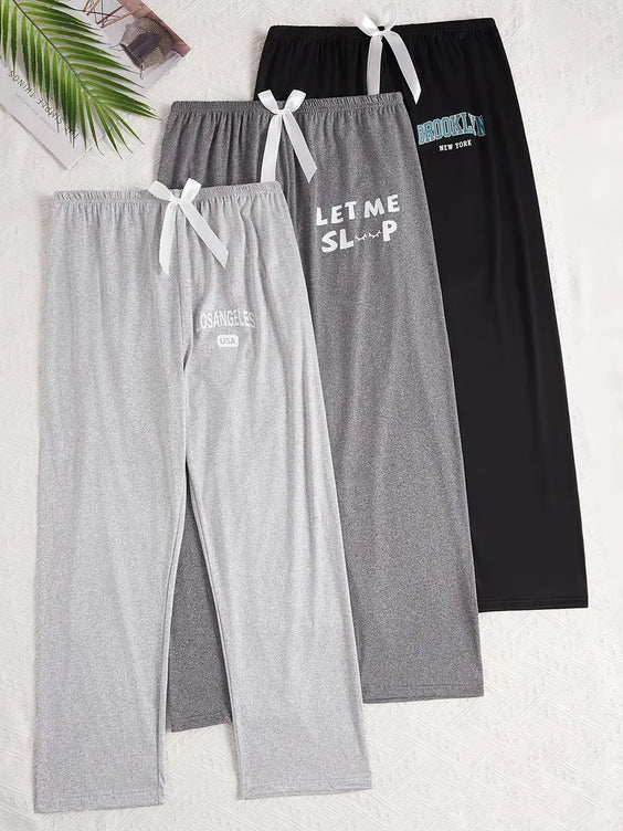 Two pairs of pajama pants, one gray and one black with text, on a white background.